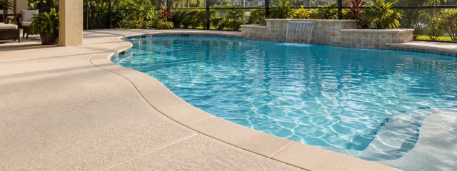 Light beige textured concrete deck around a screened backyard pool